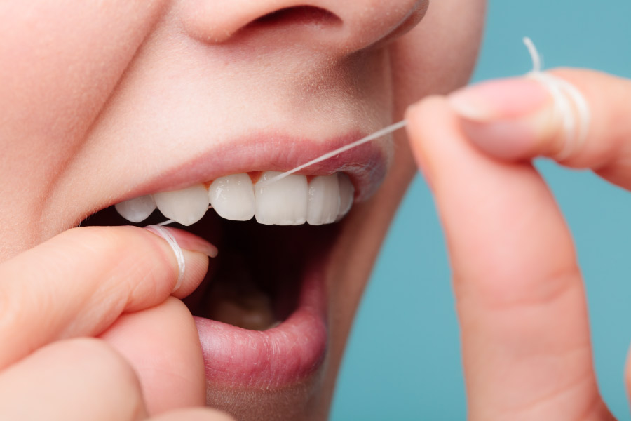 Closeup of a woman using string floss to floss between her teeth