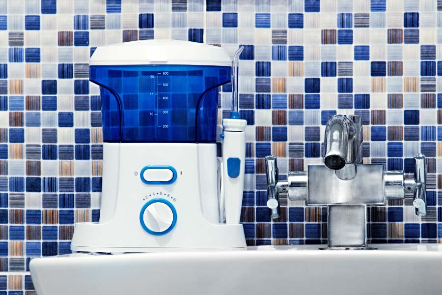 A blue and white water flosser on a bathroom counter against a blue mosaic backsplash