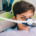 Boy sitting in the dental chair wearing a mask used to dispense nitrous oxide dental sedation.