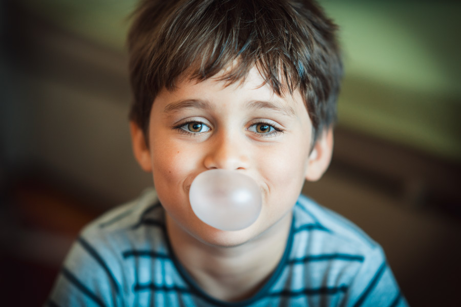 Brunette boy smiles while chewing sugar-free gum and blowing a bubble in San Antonio, TX