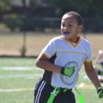 A young boy wears a sports mouthguard while playing flag football on a field outside
