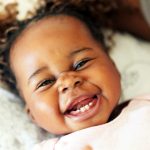 Young Black baby girl getting her baby teeth smiles while laying on the ground